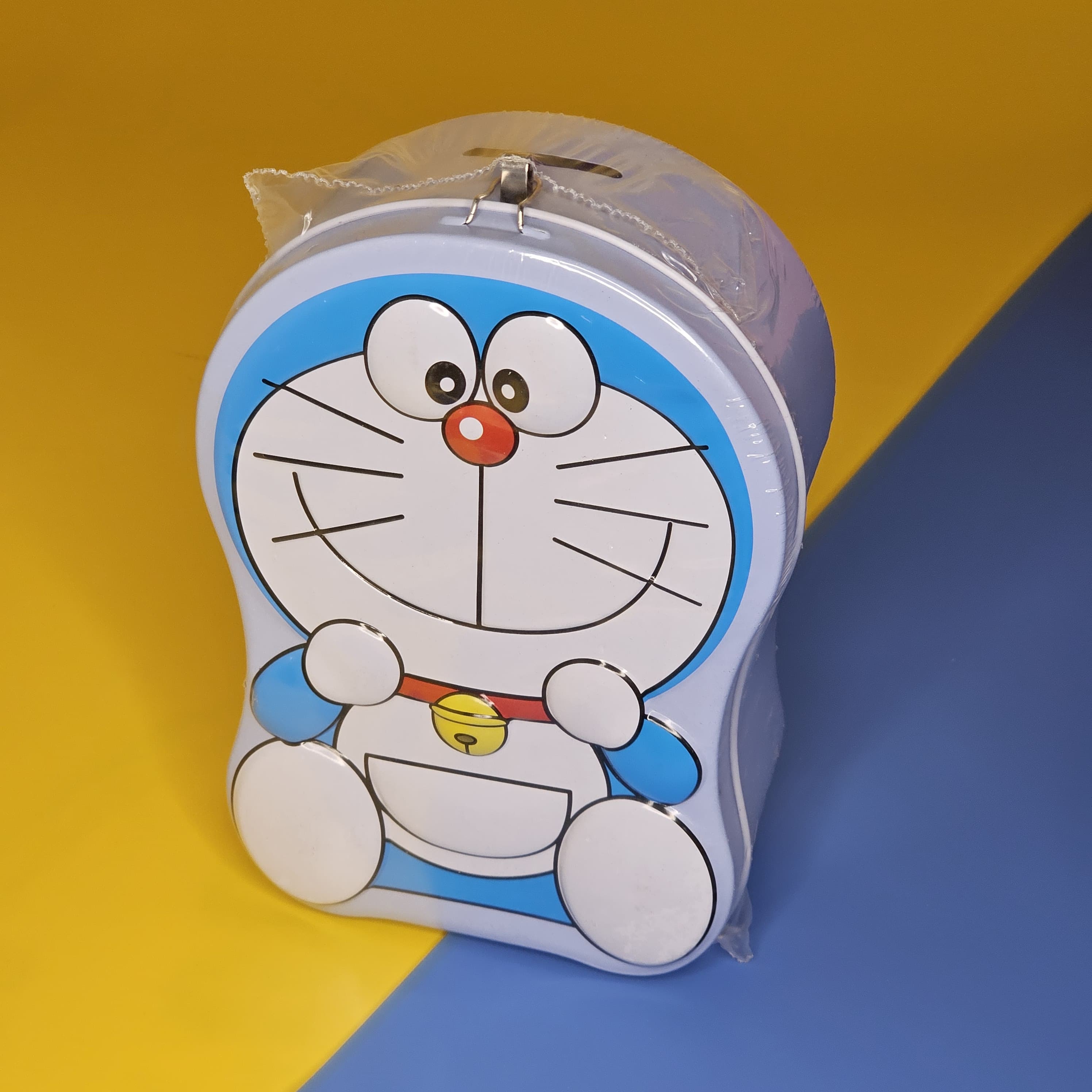 Blue and white Doraemon-shaped metal money box (piggy bank) with a top slot for coins, featuring a lock and key for secure saving. Ideal gift for kids from uSmile.toys." www.usmile.toys